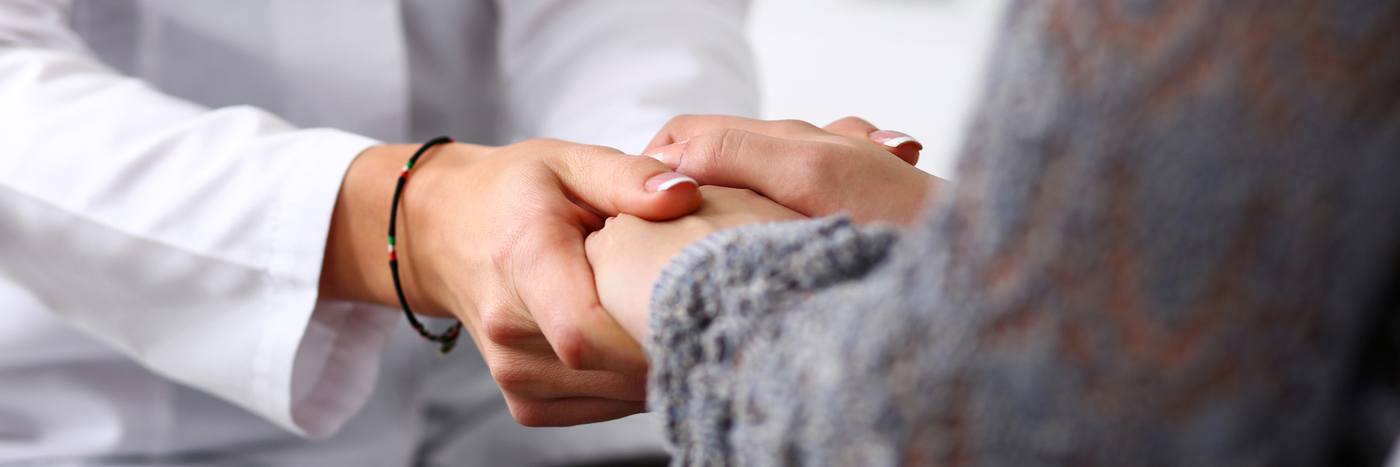 Friendly female doctor holding patient hand in office